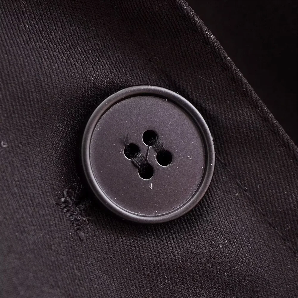 Close-up of a black four-hole button sewn onto woven fabric, highlighting the texture and stitching detail of The Noir Trench coat.