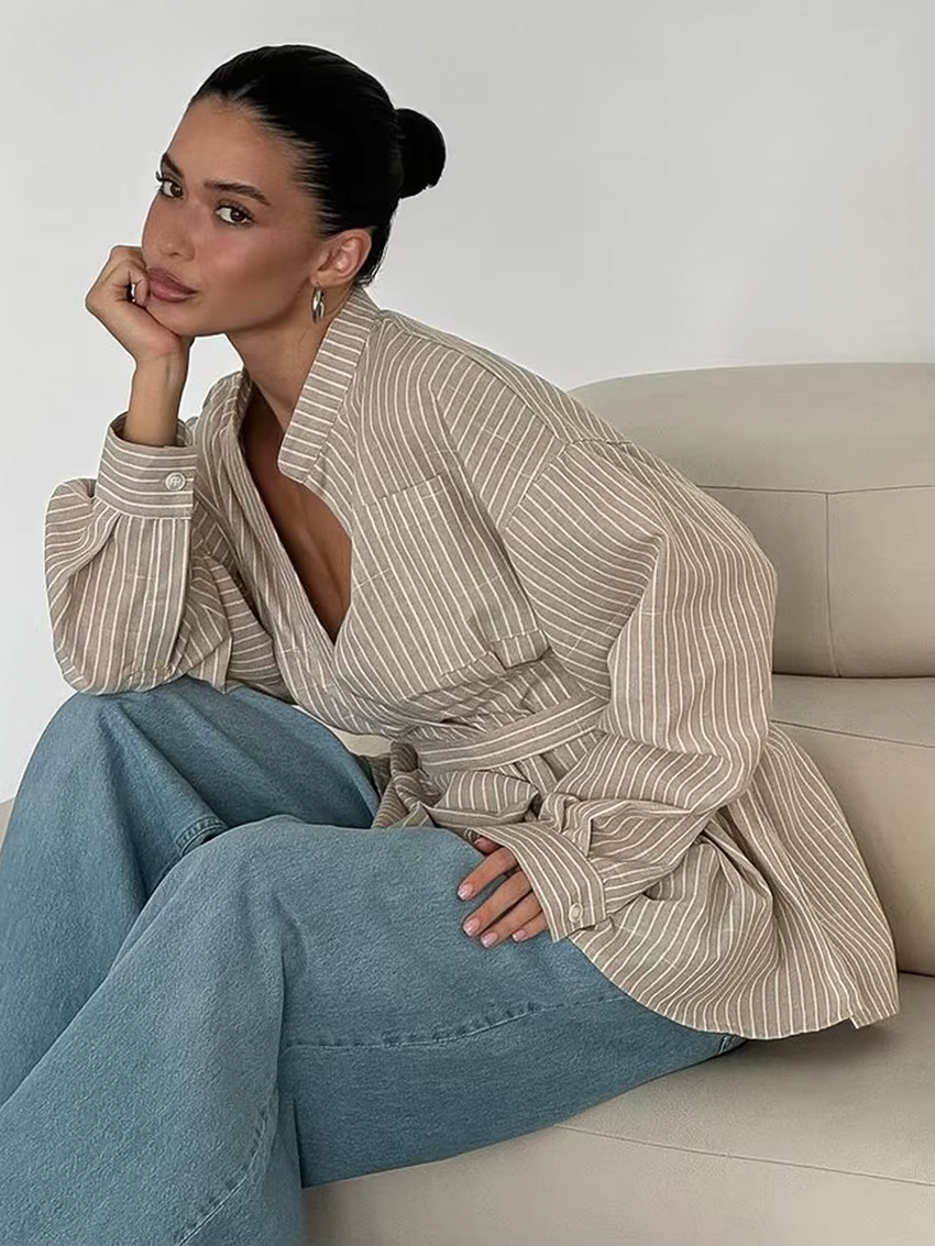 Woman sitting on a couch wearing a striped shirt and jeans in a minimalistic setting