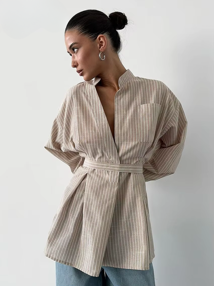 Woman wearing a beige and brown striped shirt with a belt on a plain background
