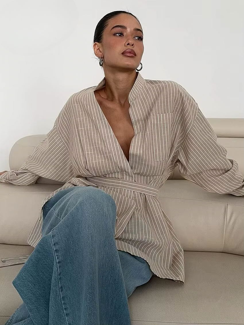Woman wearing a striped shirt and jeans sitting on a couch.
