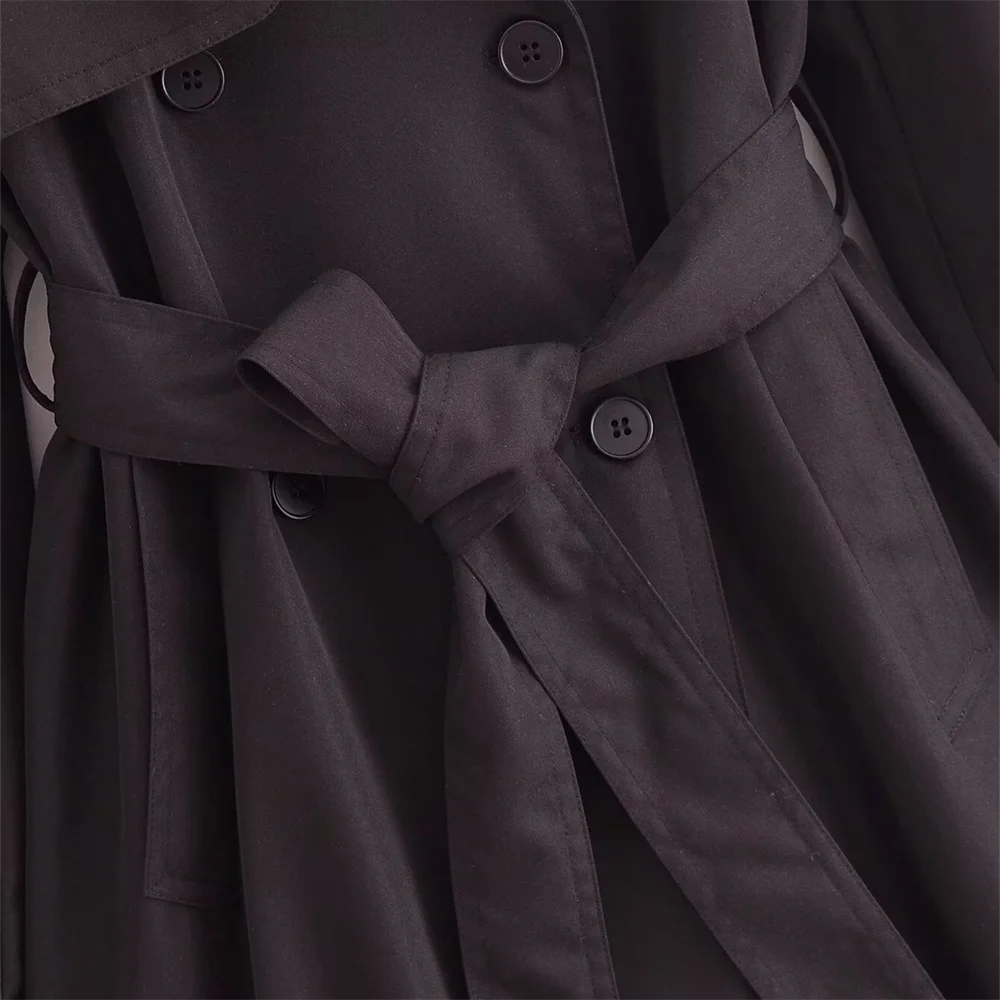 Close-up of The Noir Trench coat showing double-breasted front with button details and a tied waist belt.