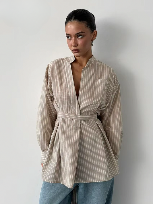 Woman wearing a beige striped shirt with a belt against a plain background